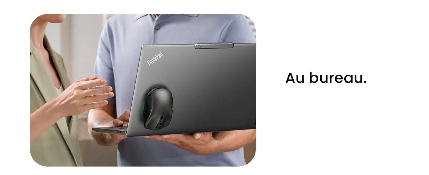 Gros plan sur deux collègues discutant dans un bureau. L'homme tient un ordinateur portable ouvert (ThinkPad) avec la souris magnétique noire attachée au dos, tandis que la femme à ses côtés semble gesticuler pour expliquer un point.