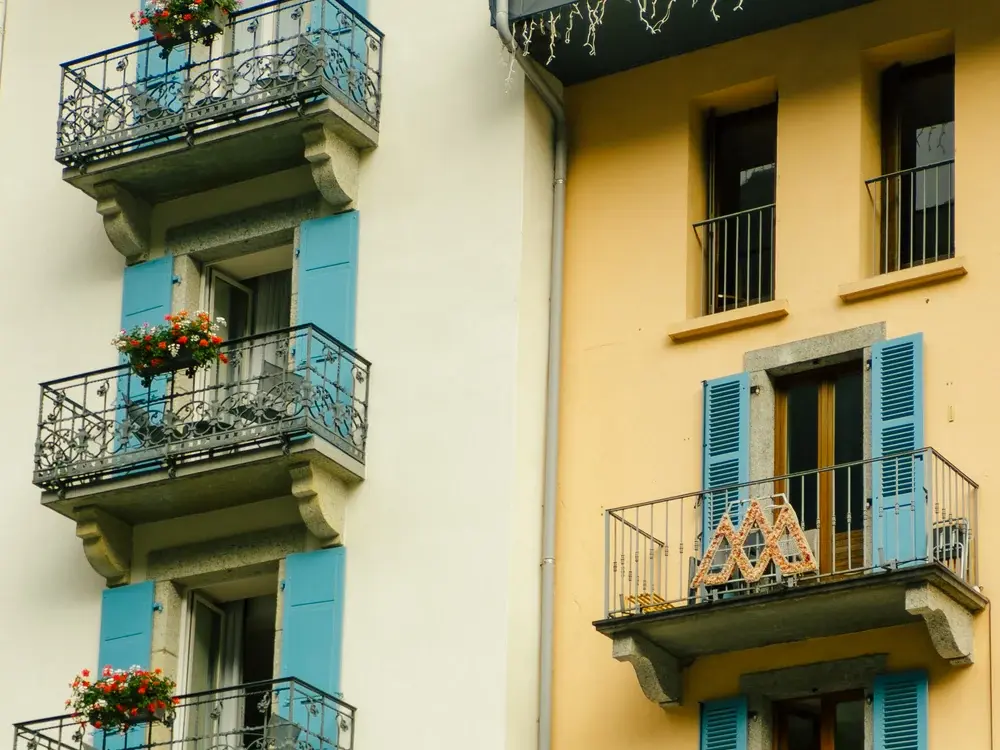 Façades d'immeubles aux volets bleus et balcons fleuris, photographiées avec le MOMENT Tele 58mm II