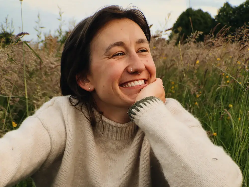 Portrait naturel d'une femme souriante en pull clair dans une prairie, réalisé avec le MOMENT Tele 58mm II