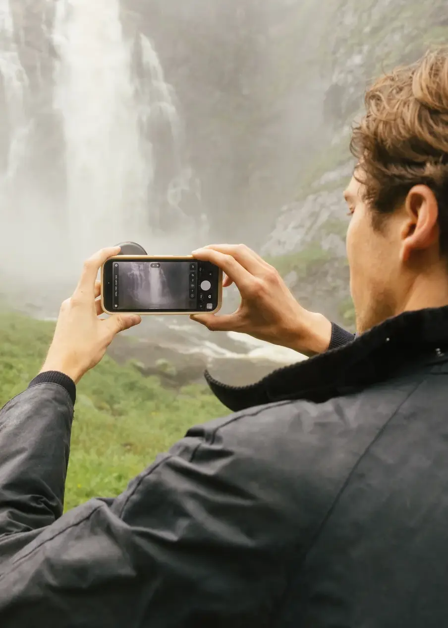 Photographe utilisant un smartphone équipé d'un objectif MOMENT devant une cascade