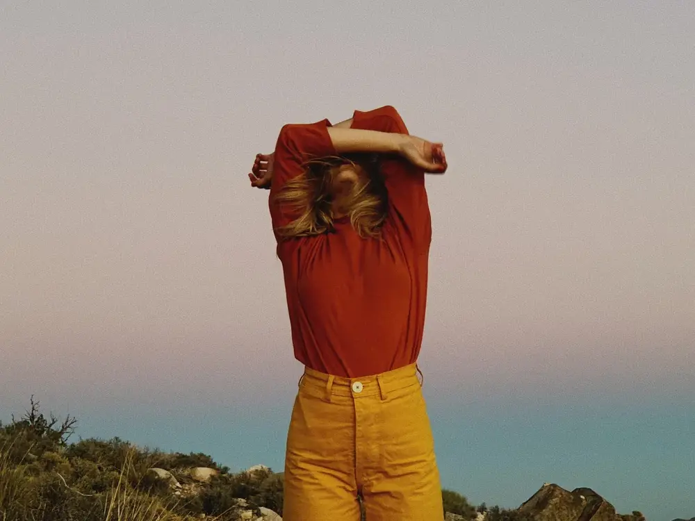 Portrait artistique d'une personne en chemise rouge et pantalon jaune dans un paysage naturel, réalisé avec le MOMENT Tele 58mm II