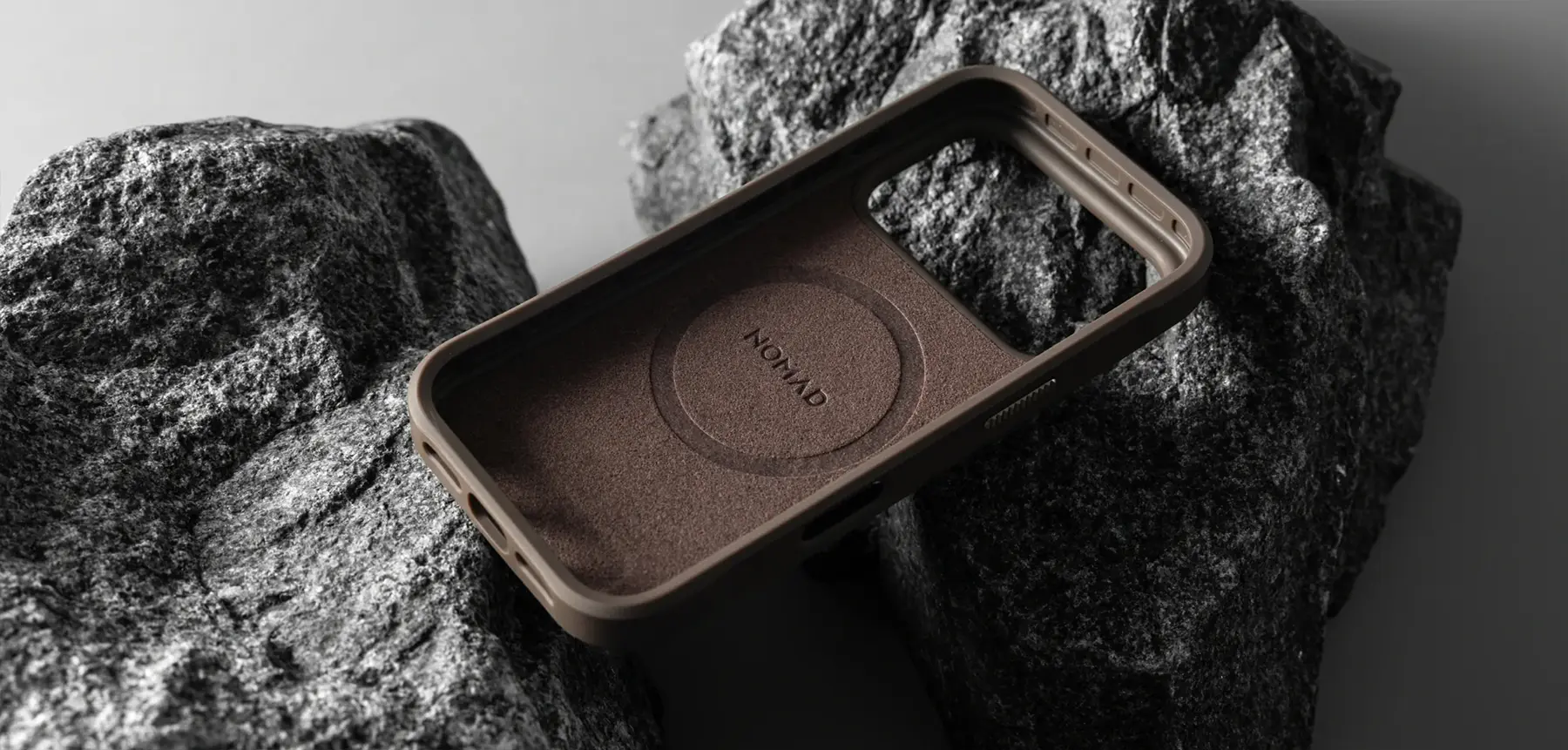 Vue intérieure de la coque NOMAD Rugged Case Arroyo marron, avec doublure protectrice en microfibre et emplacement MagSafe, posée sur des rochers