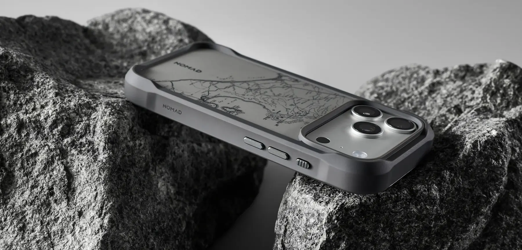 Coque MagSafe NOMAD Rugged Case Balandra beige et gris sur iPhone Pro, dos beige sable à motif cartographique, posée sur des rochers