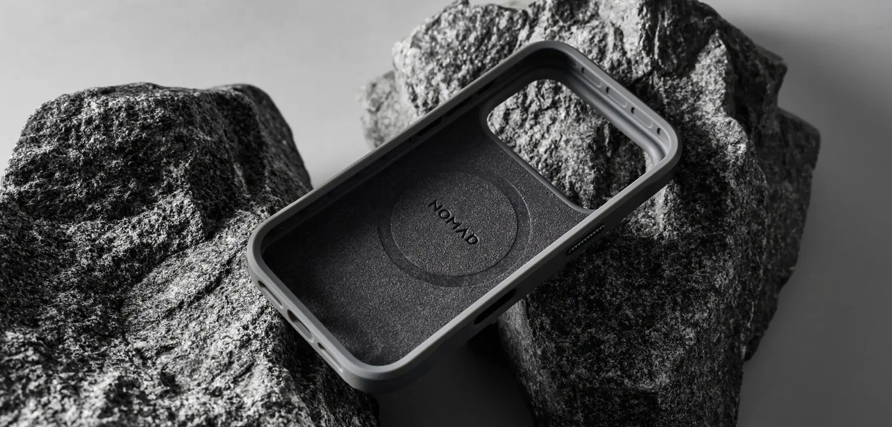 Vue intérieure de la coque NOMAD Rugged Case Balandra beige et gris, avec doublure protectrice en microfibre et emplacement MagSafe, posée sur des rochers