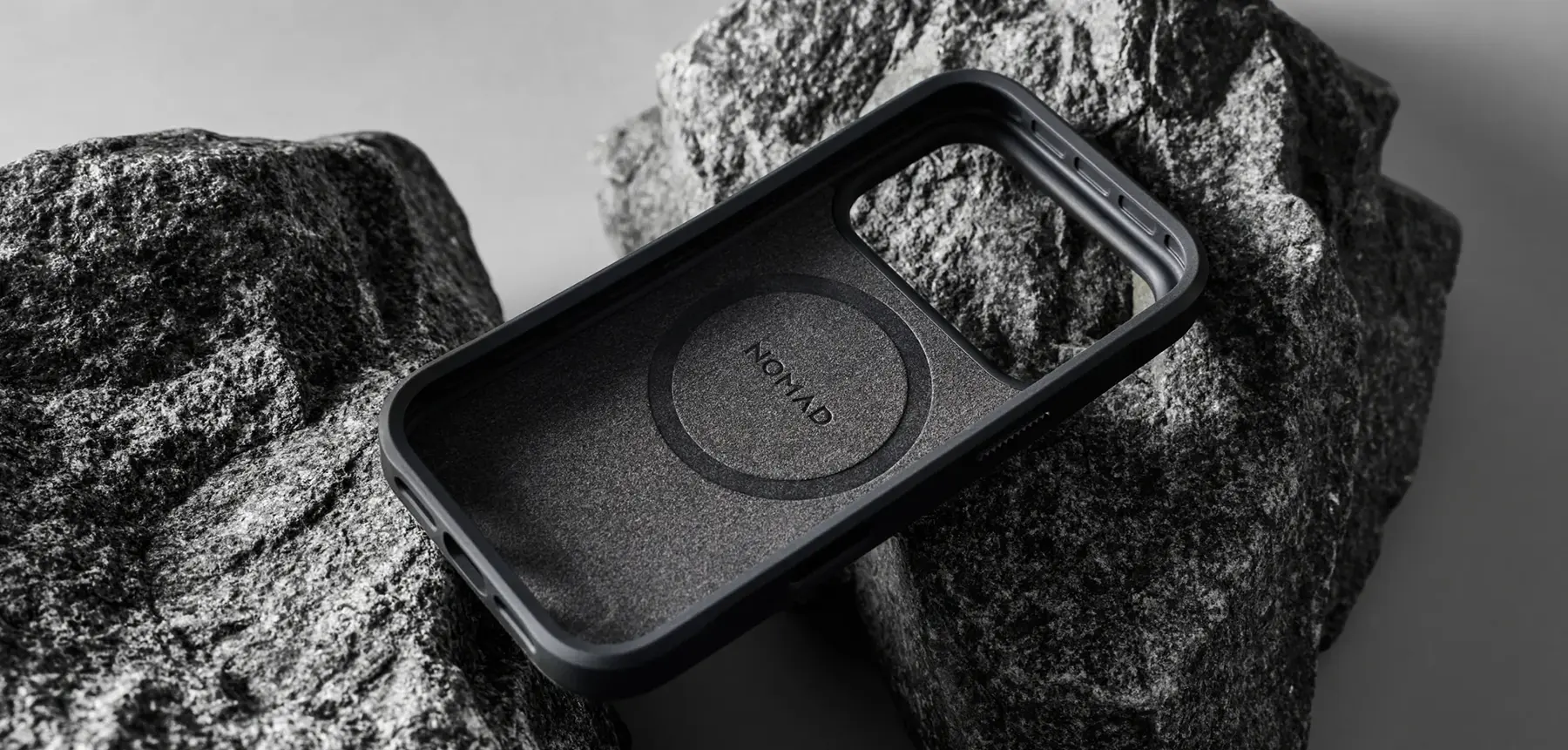Vue intérieure de la coque NOMAD Rugged Case Norte noir, avec doublure protectrice en microfibre et emplacement MagSafe, posée sur des rochers