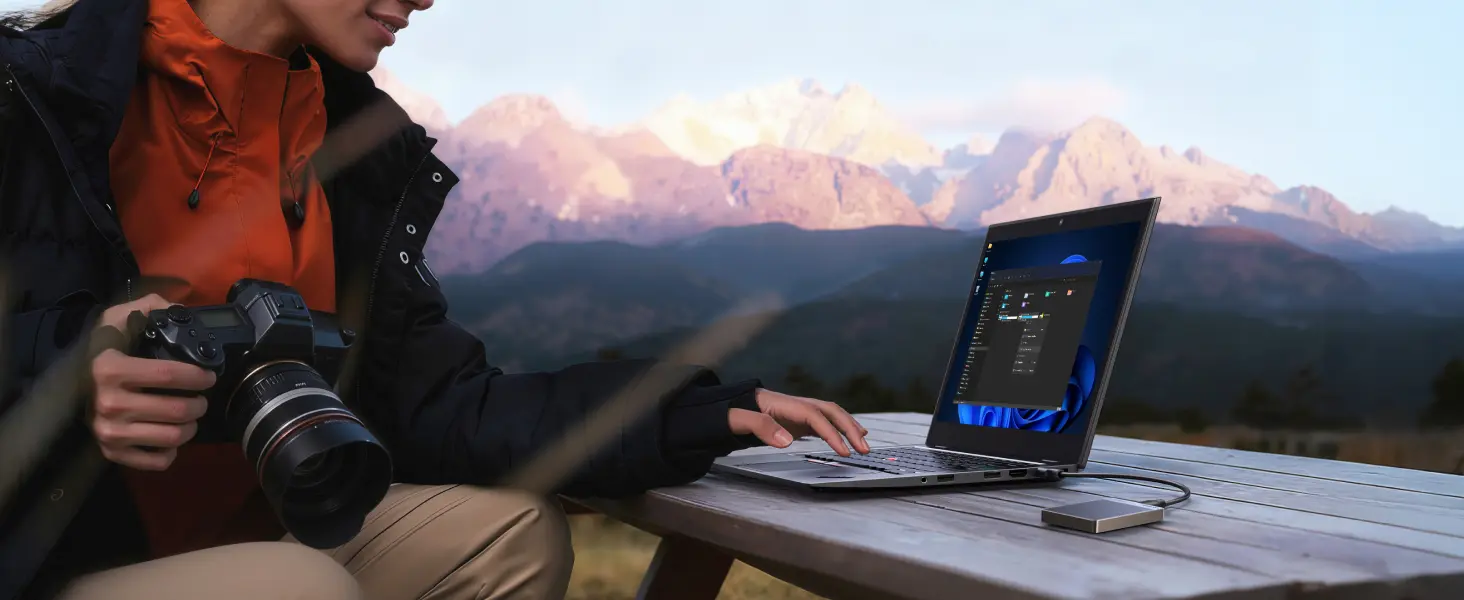 Utilisation en extérieur du SSD externe portable UGREEN 1TB branché sur un ordinateur portable par une photographe professionnelle en montagne pour le déchargement rapide de ses clichés de caméra.