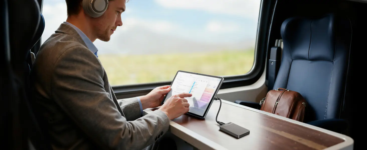 Usage en mobilité du mini SSD externe UGREEN 1TB connecté à une tablette tactile iPad par un professionnel travaillant en voyage à bord d'un train.